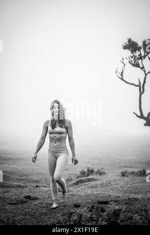 Beschreibung: Barfuß Frau in Sportbekleidung, die in nebeliger Atmosphäre über flaches Feld spaziert. Fanal Forest, Madeira Island, Portugal, Europa. Stockfoto