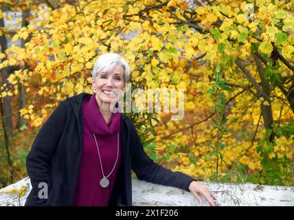 Leuchtende Farben des Herbstes in Asheville, North Carolina, umgeben diese ältere Frau, während sie sich gegen einen weißen, hölzernen Zaun lehnt. Stockfoto