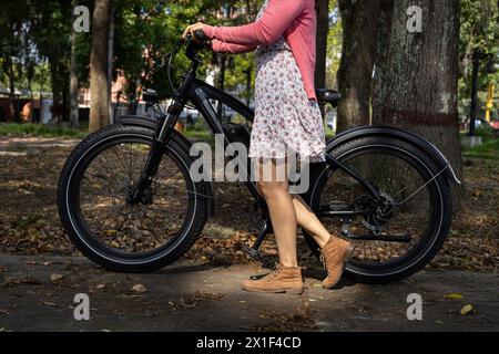 Junge Lateinamerikanerin (33) geht im Frühling mit ihrem Elektrofahrrad auf eine Fahrt. Konzeptmittel für Transport und Frühling. Stockfoto