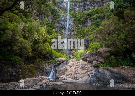 Beschreibung: Weibliche Touristin in Sportbekleidung spaziert auf Felsen am malerischen Wasserfall. Lagoa do Vento Wasserfall, Insel Madeira, Portugal, Europa. Stockfoto