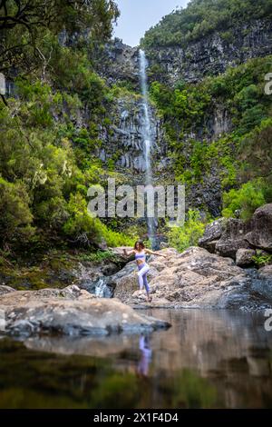 Beschreibung: Weibliche Touristen in Sportbekleidung springt über Felsen am malerischen Wasserfall. Lagoa do Vento Wasserfall, Insel Madeira, Portugal, Europa. Stockfoto