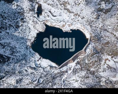 Blick von oben auf den herzförmigen See von Covão de Ferro, umgeben von Schnee. Naturpark Serra da Estrela, Manteigas, Portugal Stockfoto