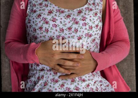 Blick von oben auf die Hände der jungen lateinamerikanischen Frau (33). Sie trägt ein Blumenkleid und einen rosa Pullover. Nicht erkennbar. Federkonzept. Stockfoto