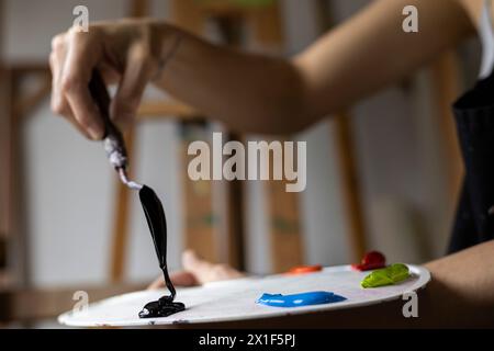 Nahaufnahme der Hände einer nicht erkennbaren lateinamerikanischen Künstlerin, die die Palette und das Palettenmesser mit den Farben zeigt, die sie in ihrer Kunstkunst verwendet Stockfoto