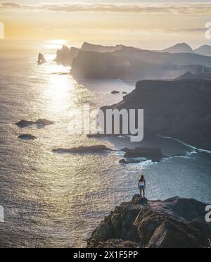 Beschreibung: Weibliche Touristen stehen am Aussichtspunkt auf einer steilen Klippe und überblicken das Meer und die zerklüfteten Ausläufer der Küste Madeiras am malerischen su Stockfoto