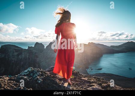 Beschreibung: Barfuß Frau in rotem Kleid genießt den Sonnenaufgang über den Ausläufern einer Vulkaninsel und dem Atlantischen Ozean. São Lourenco, Madeira Isla Stockfoto