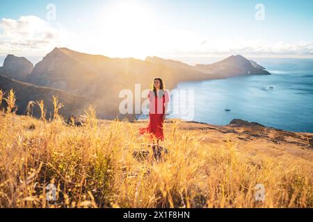 Beschreibung: Elegante Frau in rotem Kleid auf gelbem Feld genießt die morgendliche Atmosphäre über den Ausläufern einer Vulkaninsel im Atlantischen Ozean. Stockfoto