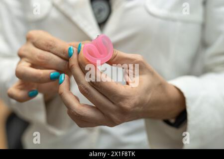 Die Hand des Arztes hält den Menstruationsbecher und zeigt, wie er richtig eingesetzt wird. Gynäkologie und Gesundheitskonzept. Stockfoto