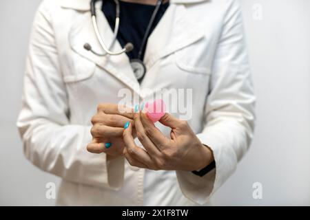 Die Hand des Arztes hält den Menstruationsbecher und zeigt, wie er richtig eingesetzt wird. Gynäkologie und Gesundheitskonzept. Stockfoto