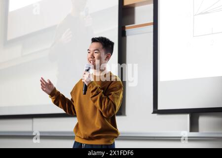 Ein Student der Universität steht vor einem Projektor in einem Klassenzimmer, hält ein Mikrofon und hält eine öffentliche Präsentation Stockfoto