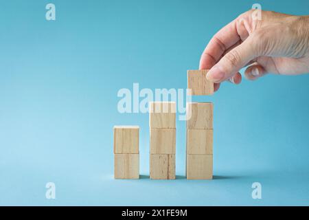 Nahaufnahme Geschäftsfrau Hand arrangiert Holzwürfel stapelnd als Treppe isoliert auf blauem Hintergrund. Kopierbereich. Stockfoto