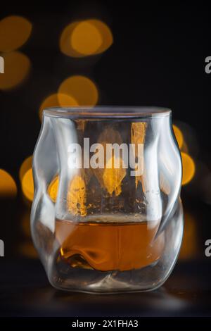 Ein Glas Alkohol sitzt auf einem Tisch. Das Glas ist halb voll und hat eine gelbliche Färbung. Das Bild hat eine warme und einladende Stimmung, was darauf hindeutet Stockfoto