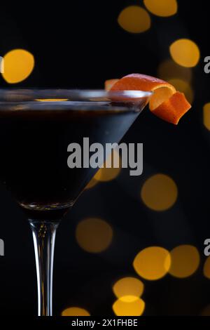 Ein Martini-Glas mit einer Orangenscheibe darüber. Das Glas ist mit einer dunklen Flüssigkeit gefüllt, und die orangefarbene Scheibe verleiht einen Farbakzent und einen Hauch von Süßigkeiten Stockfoto