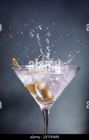 Nahaufnahme eines Actionfotos mit grünen Oliven gefüllt mit Bleu Käse, der in einen Wodka Martini geworfen wurde Stockfoto