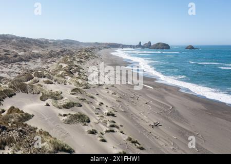 Ein Strand mit einer felsigen Küste und einem Gewässer. Der Strand ist größtenteils mit Sand bedeckt und es gibt einige Felsen verstreut. Der Himmel ist klar und klar Stockfoto