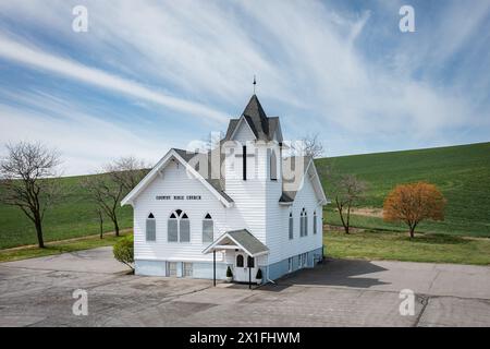 Eine kleine weiße Kirche mit einem Kreuz oben. Die Kirche ist von Bäumen und Gras umgeben. Der Himmel ist blau und im Hintergrund sind Wolken Stockfoto