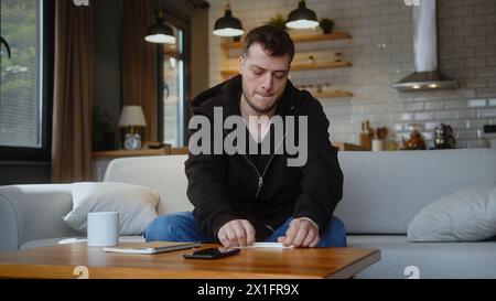 Junger Mann sitzt auf der Couch, macht Papierflugzeug und startet im Wohnzimmer zu Hause Stockfoto