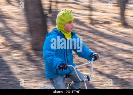 Der siebenjährige Junge fährt im Herbstpark Fahrrad. Ein Junge in blauer Jacke und gelbem Hut radelt durch einen Park Stockfoto