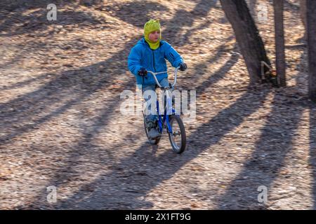 Der siebenjährige Junge fährt im Herbstpark Fahrrad. Ein Junge in blauer Jacke und gelbem Hut radelt durch einen Park Stockfoto