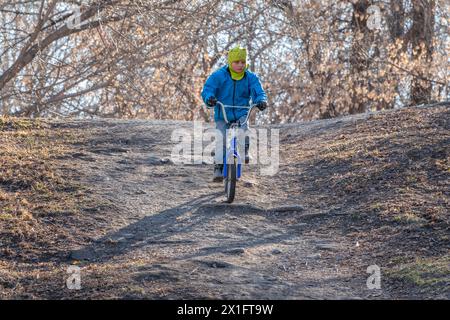 Der siebenjährige Junge fährt im Herbstpark Fahrrad. Ein Junge in blauer Jacke und gelbem Hut radelt durch einen Park Stockfoto