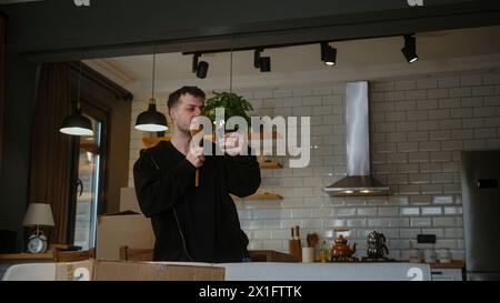 Ein Mann, der einen Blumentopf hält und wie ein Mikrofon in eine Kelle singt und zu Hause frei zur Musik tanzt, in die er gerade eingezogen ist. Stockfoto