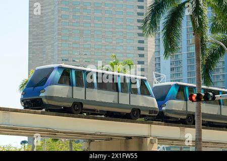 Öffentliche Verkehrsmittel im Zentrum von Miami in Florida, USA. Metrorail-Stadtzugwagen auf hoher Eisenbahn über Straßenverkehr zwischen Wolkenkratzergebäuden in Stockfoto