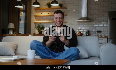 Ein fokussierter junger Mann, der ein Videospiel auf dem Smartphone spielt, während er zu Hause auf dem Sofa sitzt. Aufgeregt konzentrierter Mann, vertieft in interessantes Spiel, ha Stockfoto