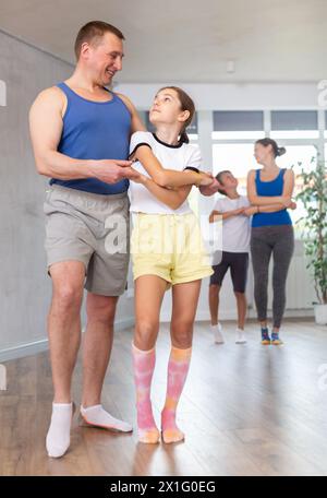 Positives Mädchen, das Tanz ausübt, bewegt sich mit dem Vater während des Tanzkurses, Familie übt Tanz zu zweit im Studio Stockfoto