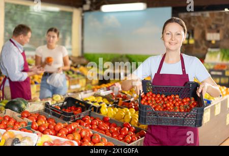 Erfolgreiche weibliche Besitzerin eines Gemüsegeschäfts, der Kiste mit Kirschtomaten hält Stockfoto