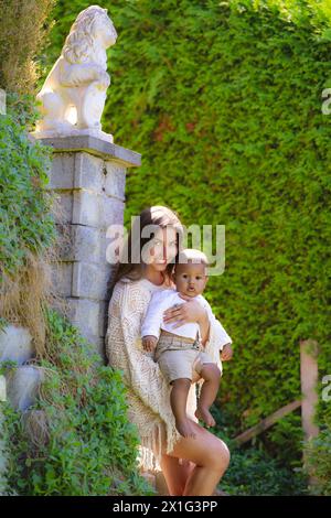 Glückliche junge Mutter, vielfältige Eltern mit Baby im Sommerhof. Überfröhliche Mutter mit einem kleinen Kind, das einen ethnischen oder multirassischen Hintergrund hat Stockfoto