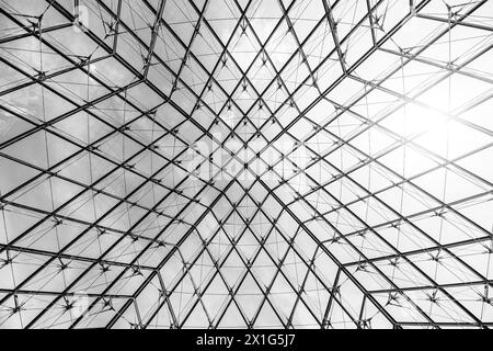 Unter der Louvre-Pyramide steht das aufwändige Glaswerk im Kontrast zum blauen Himmel an einem klaren Tag in Paris, Frankreich. Schwarzweißbild. Stockfoto