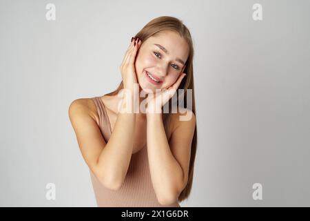 Frau posiert mit Händen auf Gesicht vor grauem Hintergrund Stockfoto