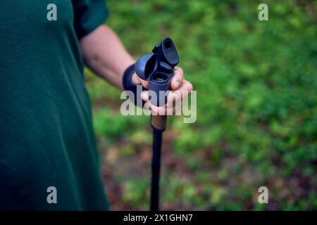 Eine ältere Frau, die im Frühlingswald mit Stöcken Nordic Walking betreibt, schaltet Musik über Kopfhörer Stockfoto