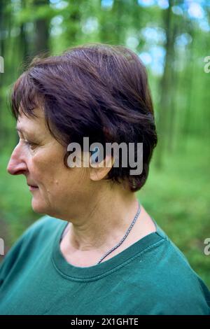 Eine ältere Frau, die im Frühlingswald mit Stöcken Nordic Walking betreibt, schaltet Musik über Kopfhörer Stockfoto