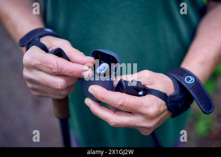 Eine ältere Frau, die im Frühlingswald mit Stöcken Nordic Walking betreibt, schaltet Musik über Kopfhörer Stockfoto