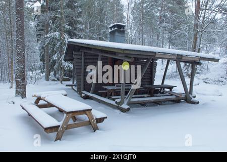 Schneebedeckte Holzkochhütte mit Tisch und Kamin in Vetokannas bei bewölktem Winterwetter, Porkkalanniemi, Kirkkonummi, Finnland. Stockfoto