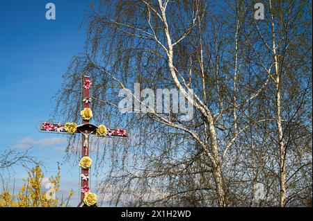 Ein Straßenkreuz, dekoriert mit Blumen im Frühjahr auf einem Schrein am Straßenrand vor dem Hintergrund von Birkenzweigen Stockfoto