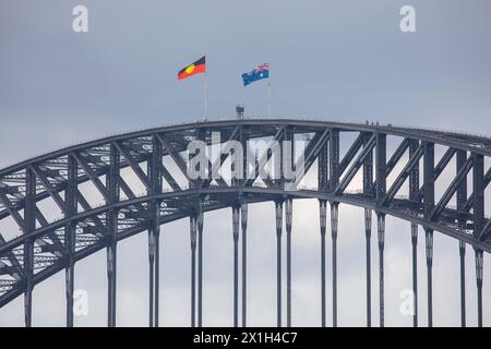 Die berühmte Sydney Harbour Bridge, die Flaggen der Aborigines und australiens, die auf dem Gipfel fliegen, die Menschen, die den Bogen vom Brückenkletterausflug hinunterlaufen, Sydney, NSW Stockfoto