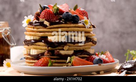 Pfannkuchen mit Banane, Heidelbeeren, Erdbeeren und Schokoladensauce auf einem Teller. Stockfoto
