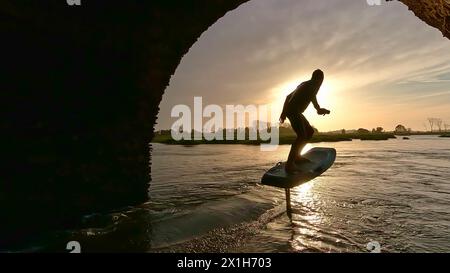 Tragflächenreiter gleitet mit seinem Brett in einem der Kanäle der Ria de Aveiro in Portugal während des Sonnenuntergangs über dem Wasser. Stockfoto