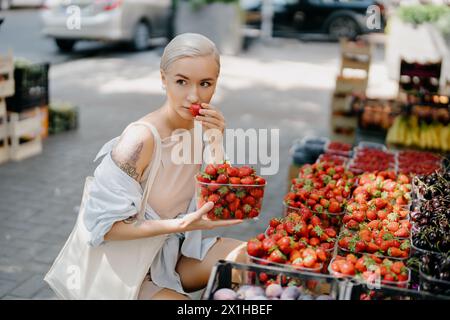 Eine junge Frau, die frische Erdbeeren auf einem lokalen Markt genießt Stockfoto