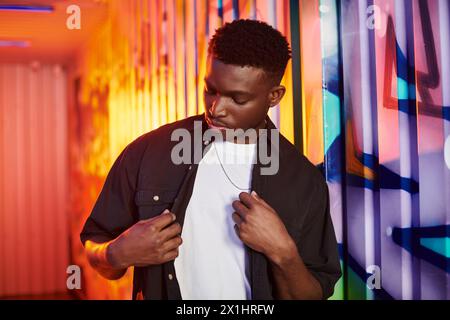 Ein Mann steht selbstbewusst vor einer lebendigen, bunten Mauer in einer urbanen Umgebung. Stockfoto