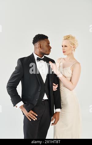 Eine wunderschöne blonde Braut in einem Hochzeitskleid und ein Afroamerikaner im Smoking nebeneinander stehen. Stockfoto