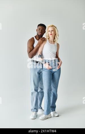 Ein junges multikulturelles Paar, das in einem Studio vor grauem Hintergrund zusammen steht und Einheit und Vielfalt zeigt. Stockfoto