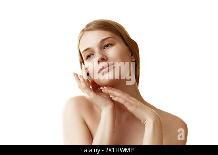 Junge schöne Frau mit nackten Schultern, die sanft ihr Gesicht berührt und es vor weißem Studiohintergrund umrahmt. Stockfoto