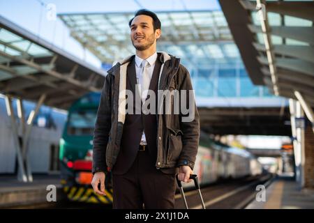 Ein schicker Mann im Business-Anzug wartet auf einem sonnigen Bahnsteig auf seinen Zug Stockfoto