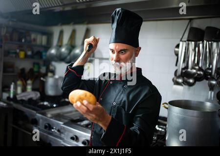 Der konzentrierte Koch in Uniform untersucht eine Kartoffel in einer professionellen Küche Stockfoto