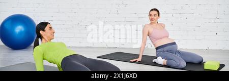 Zwei Frauen, eine schwangere, spielen anmutig Yoga-Posen in einer ruhigen Umgebung, die von einem Lehrer während eines Elternkurses geführt wird. Stockfoto