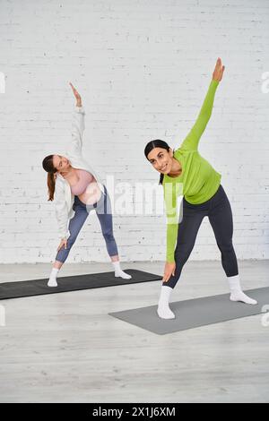 Eine schwangere Frau praktiziert anmutig Yoga mit ihrem Lehrer in einer ruhigen Studioumgebung. Stockfoto