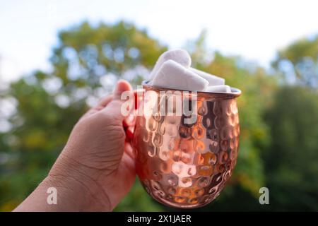 Kupferbecher trinken Kaffee Cappuccino, heiße Schokolade mit Marshmallows in weiblicher Hand, stimuliert das Nervensystem, gesundheitliche Vorteile und Schäden Stockfoto